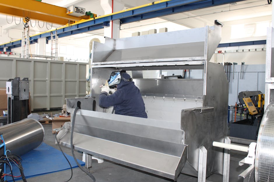 A worker welds metal components inside a large industrial factory.