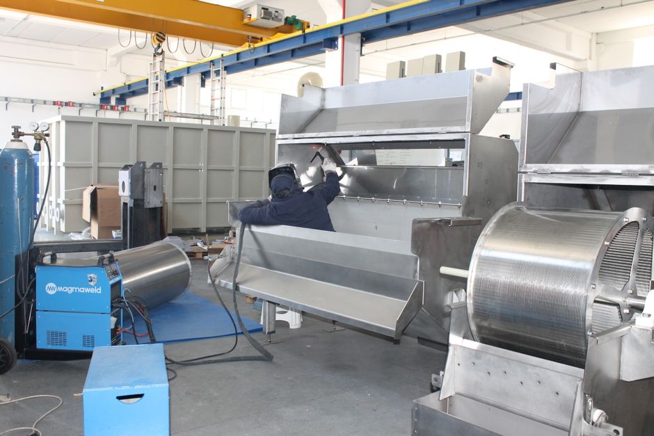 A worker welds metal machinery inside an industrial facility, showcasing production processes.