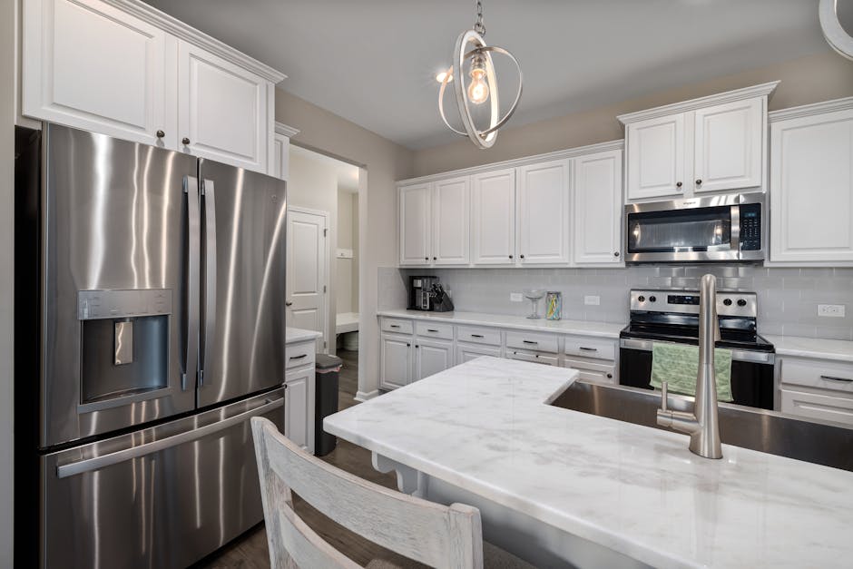 Elegant modern kitchen featuring white cabinetry and stainless steel appliances with marble countertops.