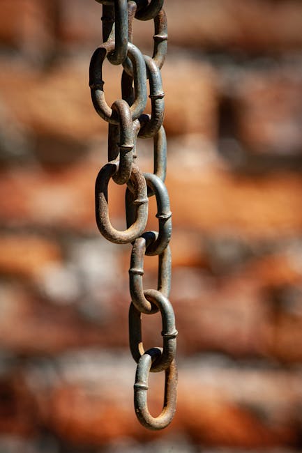 Detailed close-up of a rusty metal chain hanging against a blurred brick wall in Mérida, Venezuela.