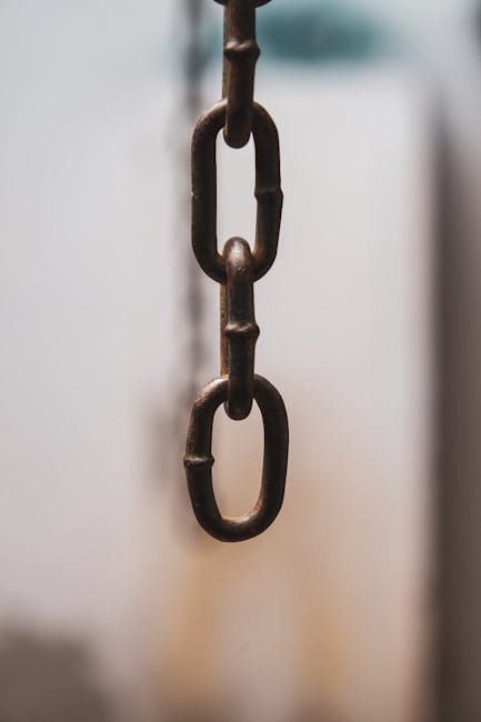 Detailed view of an iron chain link hanging vertically with a soft focus background.