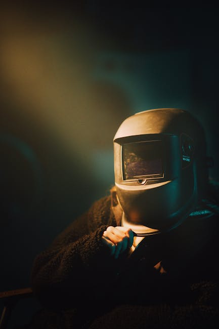 A person wearing a welding helmet in dark, moody lighting suggests mystery and introspection.
