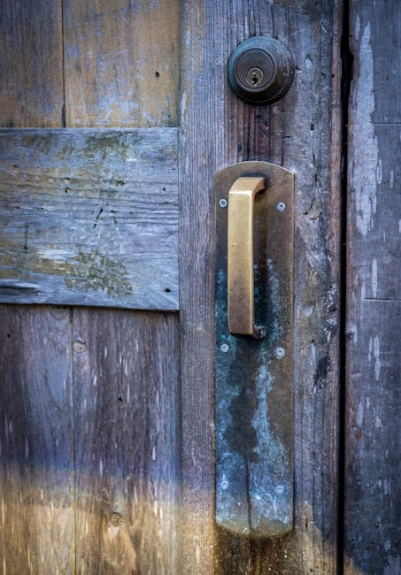 Close-up of a weathered wooden door featuring a rustic brass handle and keyhole.