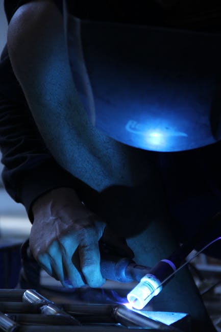 Detailed view of a welder working with a blue arc light in an industrial environment.
