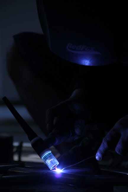 A welder focusing on his task, illuminated by blue light at night.