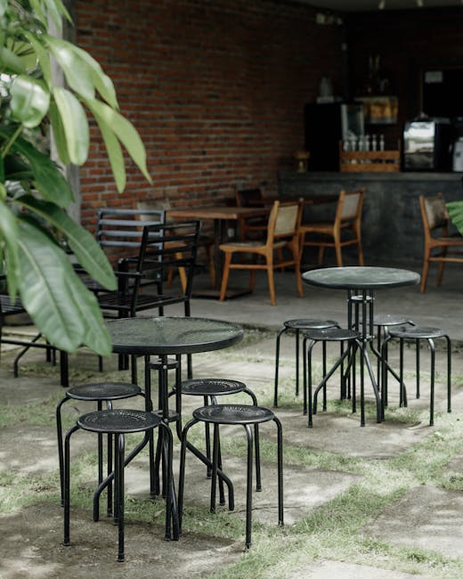 A charming outdoor bistro setting with empty tables and metal chairs surrounded by lush greenery.
