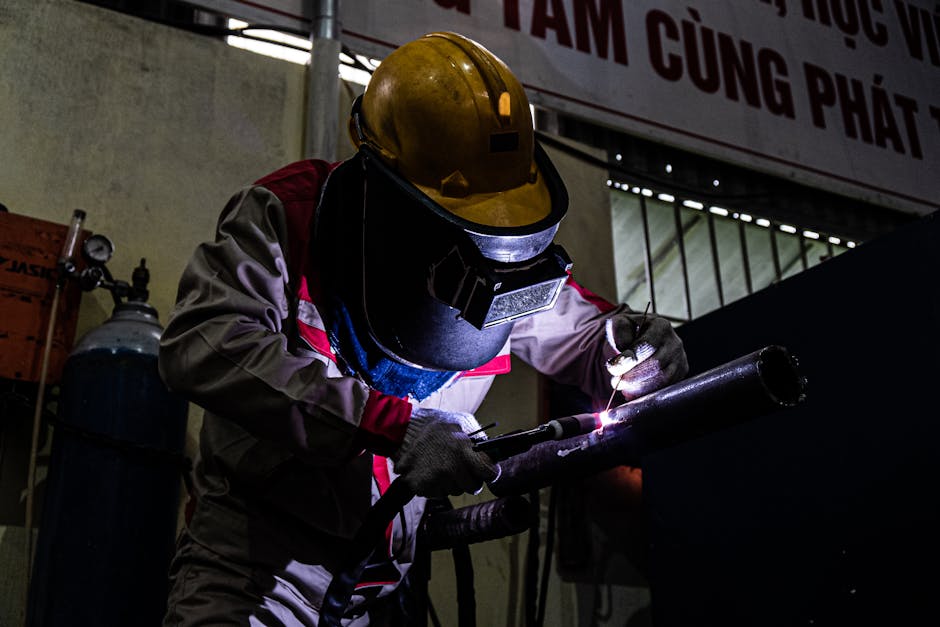 A welder skillfully working in a dimly lit industrial setting, using protective gear and equipment.