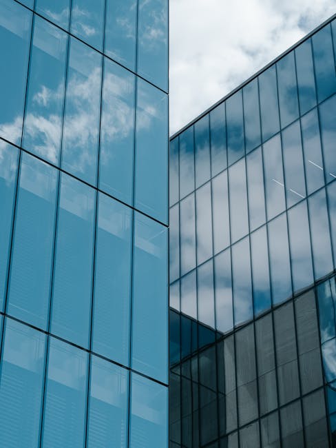 A low-angle shot of a contemporary glass skyscraper reflecting the sky and clouds.