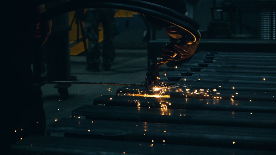 Industrial scene with worker cutting steel, producing dynamic sparks in a factory environment.