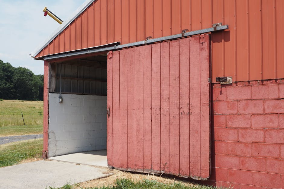 Open red barn with sliding wooden door on a rural farm landscape.