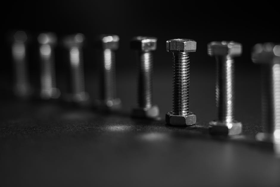 A black and white image focusing on metal bolts arranged in a row with shallow depth of field.