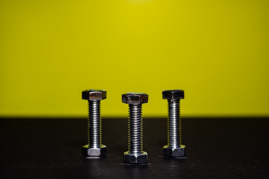 Close-up image of three steel bolts standing upright against a contrasting yellow background.