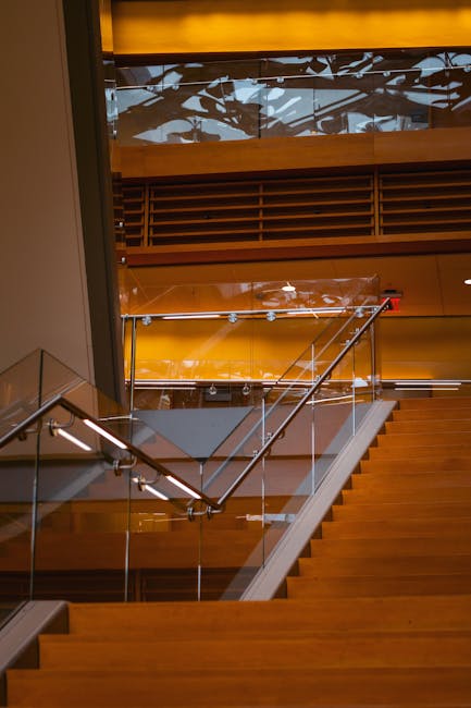 A sleek modern staircase with wooden steps and glass railing inside a contemporary building.