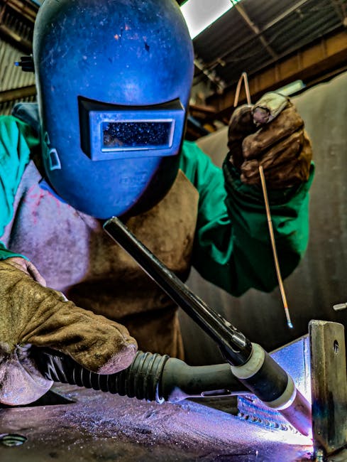 Welder in protective gear focusing on welding task with bright sparks in an indoor setting.