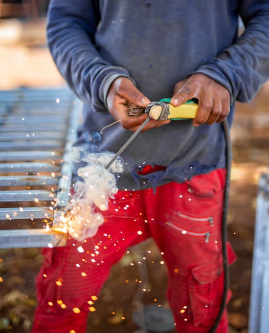 A welder in protective gear creating sparks while welding metal outdoors.