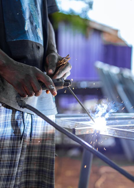 A welder skillfully crafts metal with bright sparks flying around in an outdoor workspace.