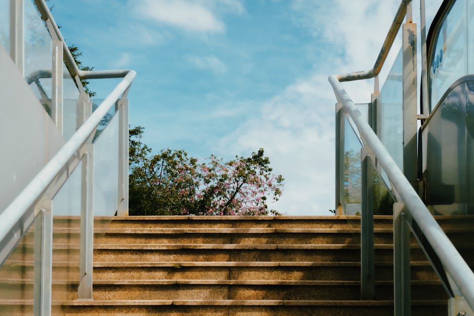 A serene stairway in the city leading towards blue skies and greenery, evoking urban escape.