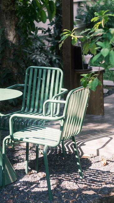 Green metal chairs and table on a sunlit patio surrounded by lush foliage.