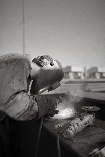 A welder with protective gear operating in an outdoor industrial setting.