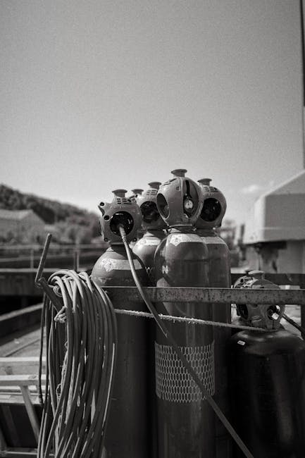 Black and white image of industrial gas cylinders and hoses outdoors on a construction site.