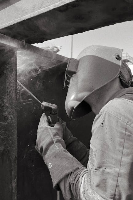 A welder in protective gear working on a metal structure.