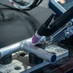 Detailed view of metal welding apparatus in action on industrial workbench.