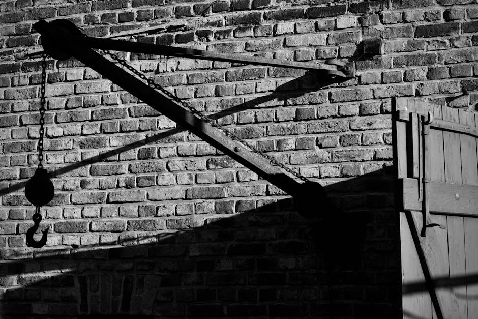 Monochrome industrial hook and pulley on a rustic brick wall, casting shadows.