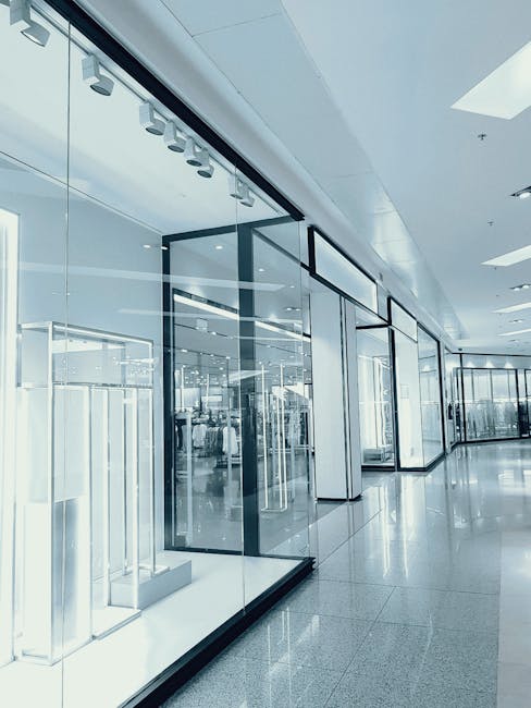Bright and empty shopping mall corridor with glass display walls and reflections.