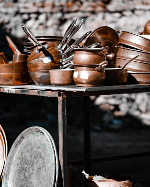 Collection of vintage copper pots and pans on an outdoor rustic table.