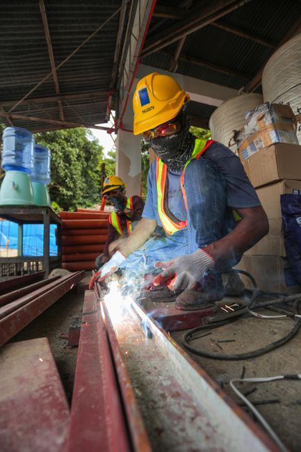 Construction worker welding metal beams outdoors with safety gear and hard hat.