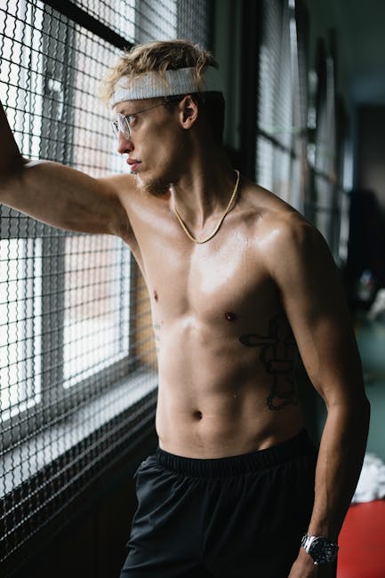 Confident shirtless tattooed male in glasses and headband standing near metal lattice and looking in window