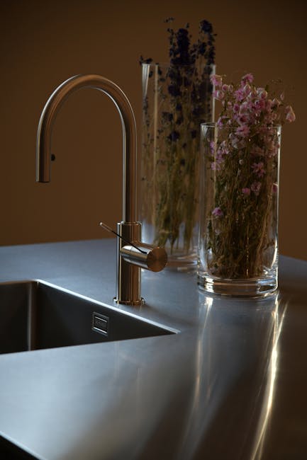 A modern stainless steel sink with glass jars filled with flowers.