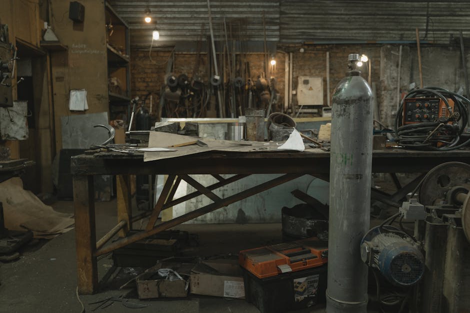 A cluttered blacksmith workshop showcasing various tools, metalworking equipment, and a rustic, industrial atmosphere.