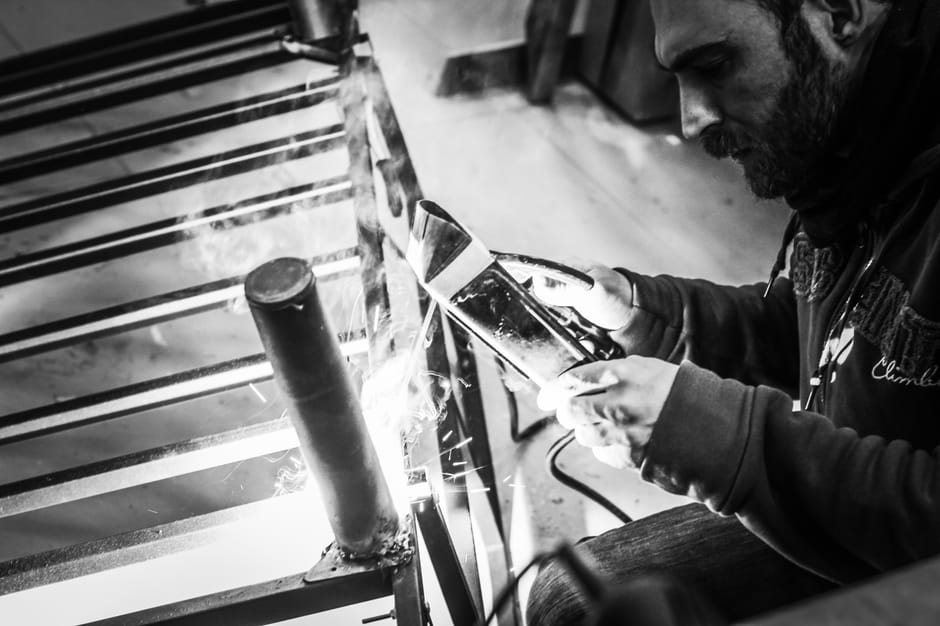 Black and white image of a man welding metal, showcasing focus and craftsmanship.