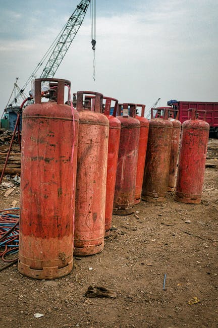 Lange aged red gas tanks placed on dry ground in industrial area in daytime