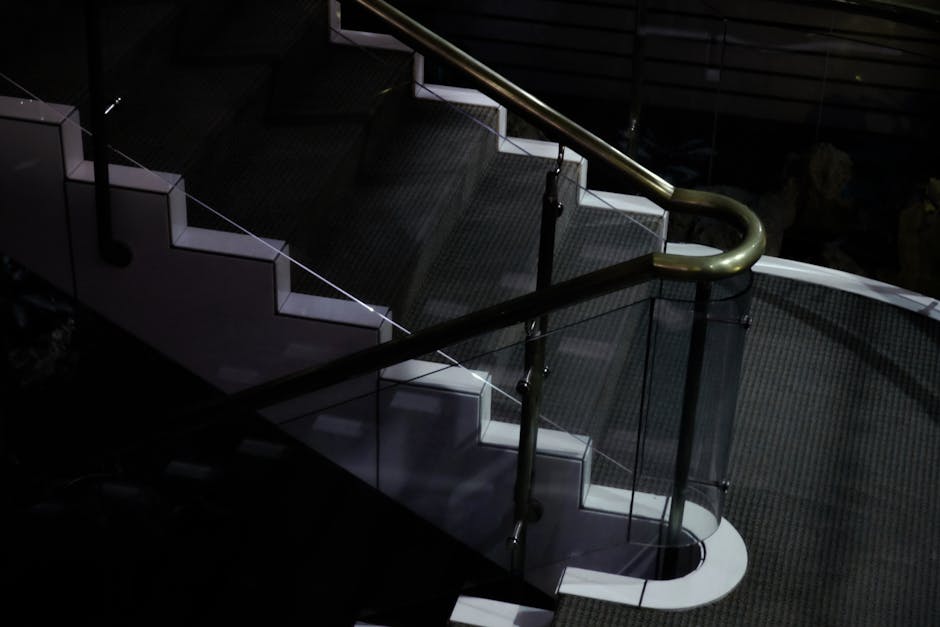 A sleek and modern glass staircase with a metal handrail in a dimly lit environment.