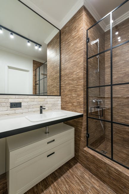White cabinet under sink at wall with mirror near glass shower cabin in modern stylish bathroom with glowing lights in apartment