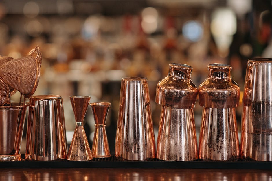 Close-up of copper bartending tools on the counter with a blurred bar background.