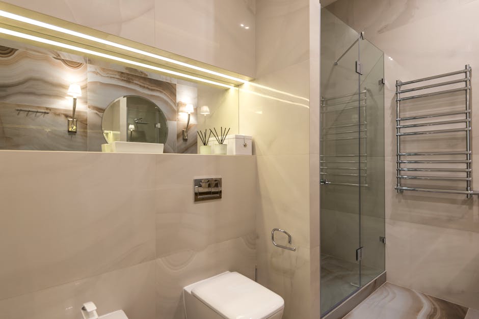 A contemporary bathroom with marble tiles, glass shower, and LED lighting.