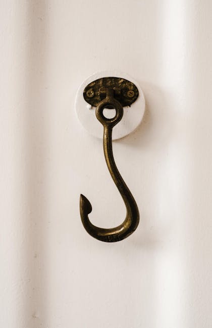 Close-up of a vintage brass hook mounted on a white wall, highlighting texture and detail.