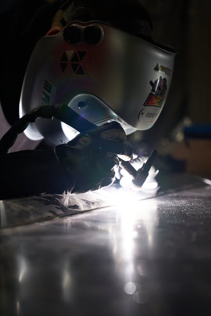 Close-up of a welder in action, wearing protective gear and welding metal indoors.