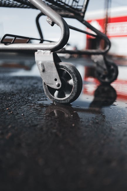 Focused close-up of a shopping cart wheel on wet asphalt, reflecting light.